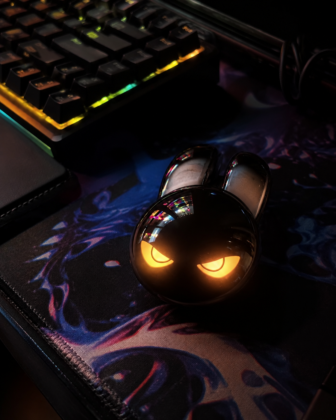 Evil bunny wireless mouse with orange glowing eyes beside an RGB gaming keyboard