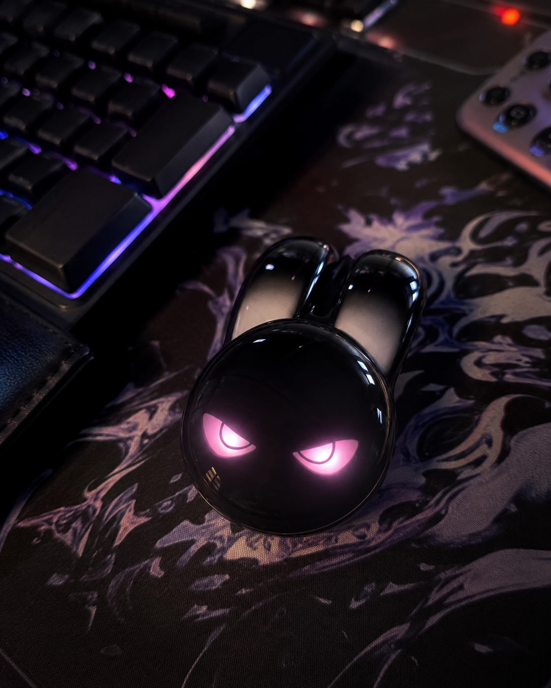 Black evil bunny wireless mouse with glowing pink eyes on a dark floral desk mat