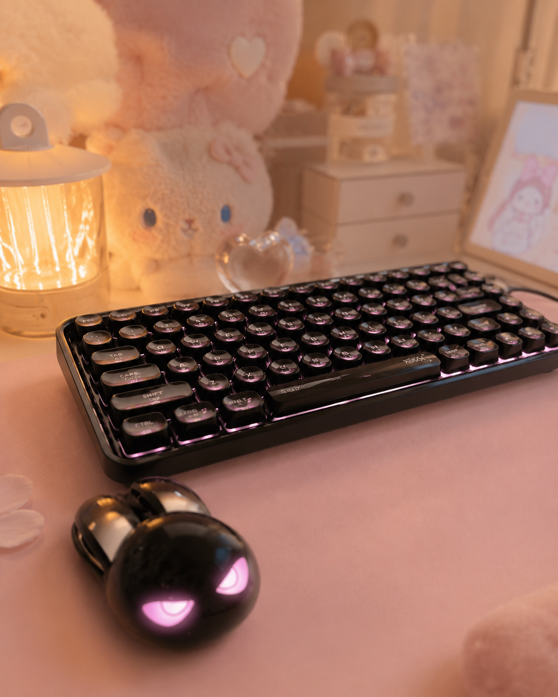 Black bunny-shaped wireless mouse with pink glowing eyes on a pastel desk with plush toys